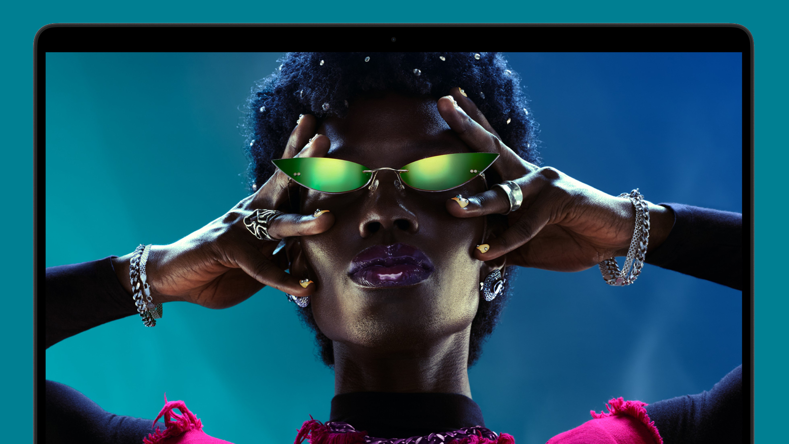 An Apple MacBook Pro M6 on a green background showing the face of a woman wearing sunglasses