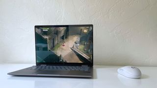 The HP Envy x360 2-in-1 on a white desk beside a white mouse with the game Death&#039;s Door on screen