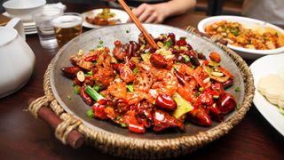 Close up image of a person with chopsticks as they dive into Szechwan dry hotpot with chicken wing and prawn.