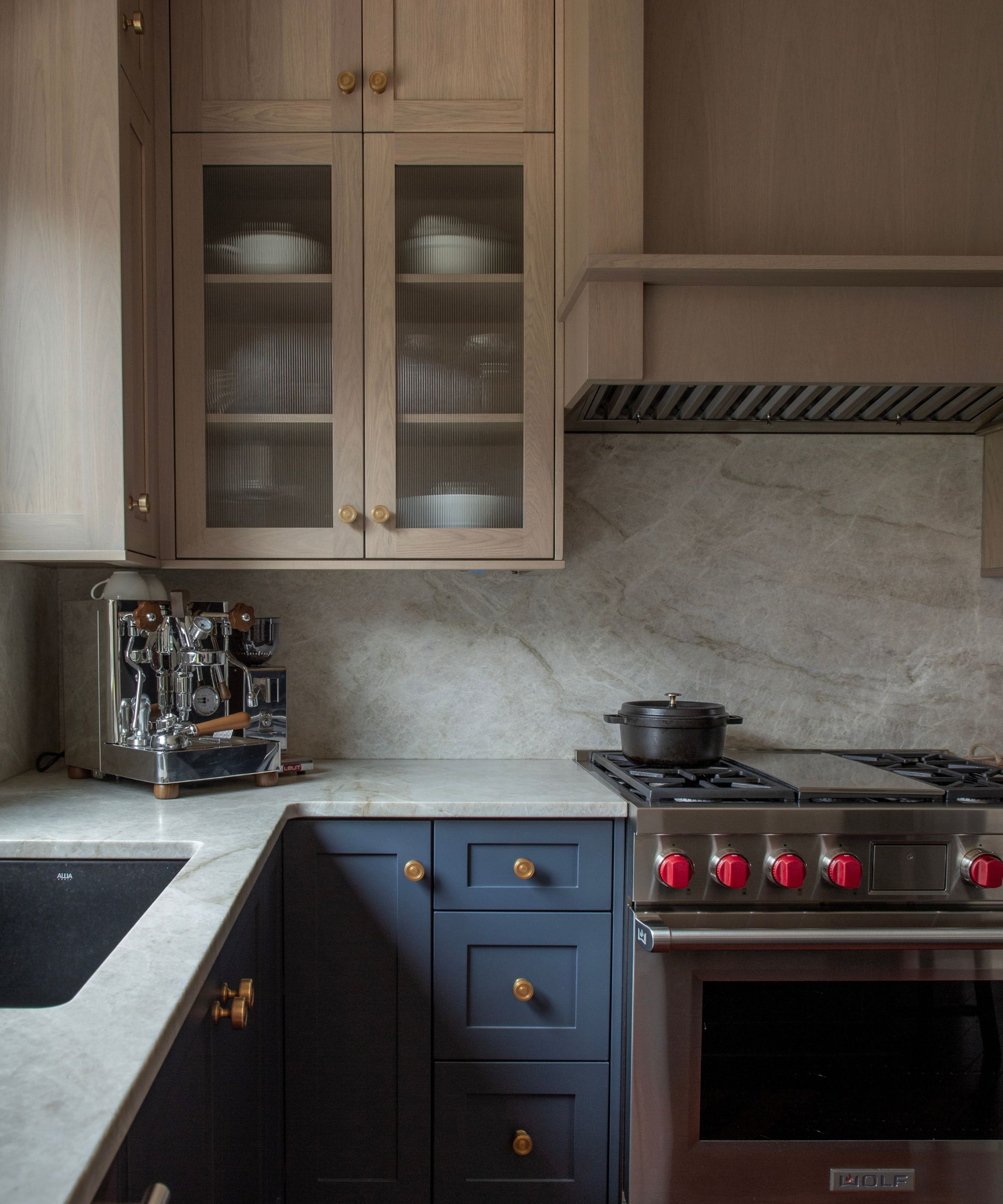 Kitchen corner featuring fluted glass cabinet doors, light wood upper cabinets, dark blue lower drawers with gold knobs, and a professional stainless steel range.
