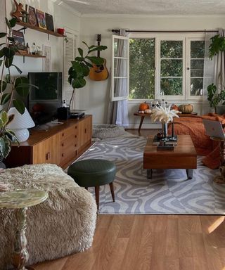 A small living room with a TV on a wooden TV stand, a coffee table, rug, couch, and fluffy footrest