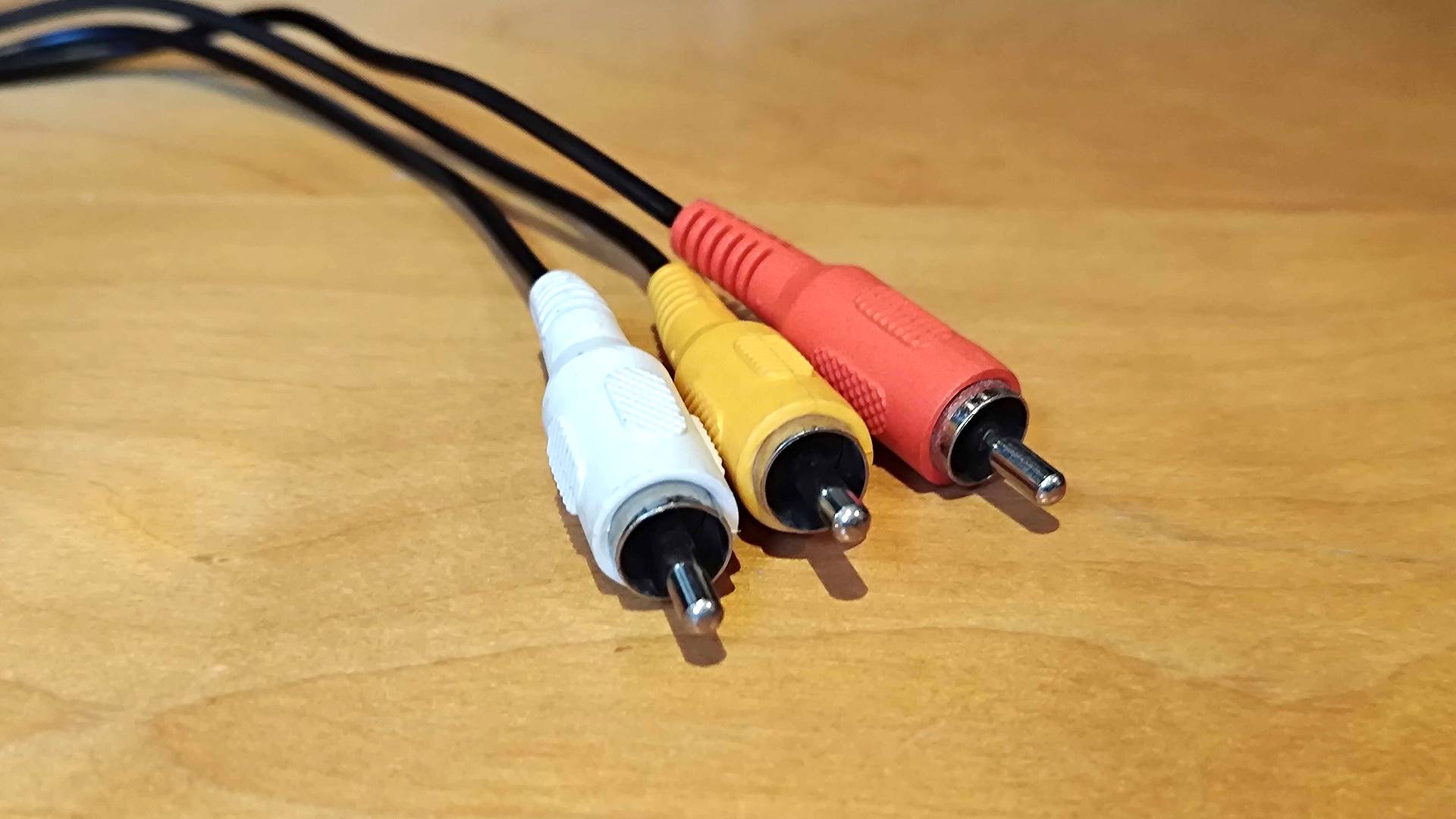 RCA composite cables in red, yellow, and white on woodgrain desk.