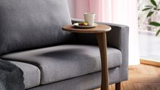 IKEA UGGLERUM Side Table in Brown in front of gray sofa with mug on top, pink sheer curtains, and timber floor
