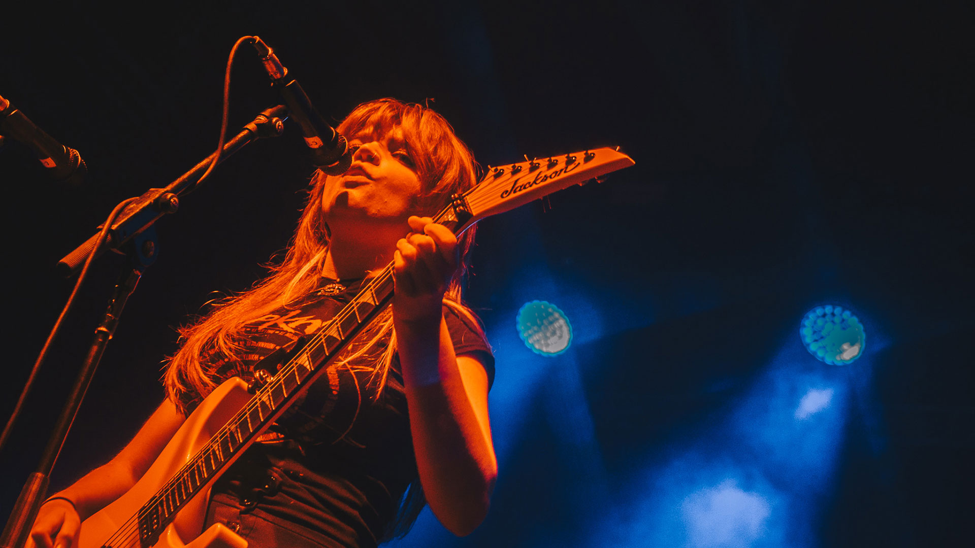Debbie Gough under orange stage lighting, playing her Jackson electric guitar