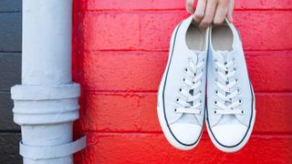 A pair of white shoes held over a red wall
