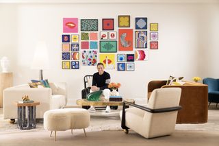 A living room with Jonathan Adler sat on a chair and colorful modular artwork on the wall