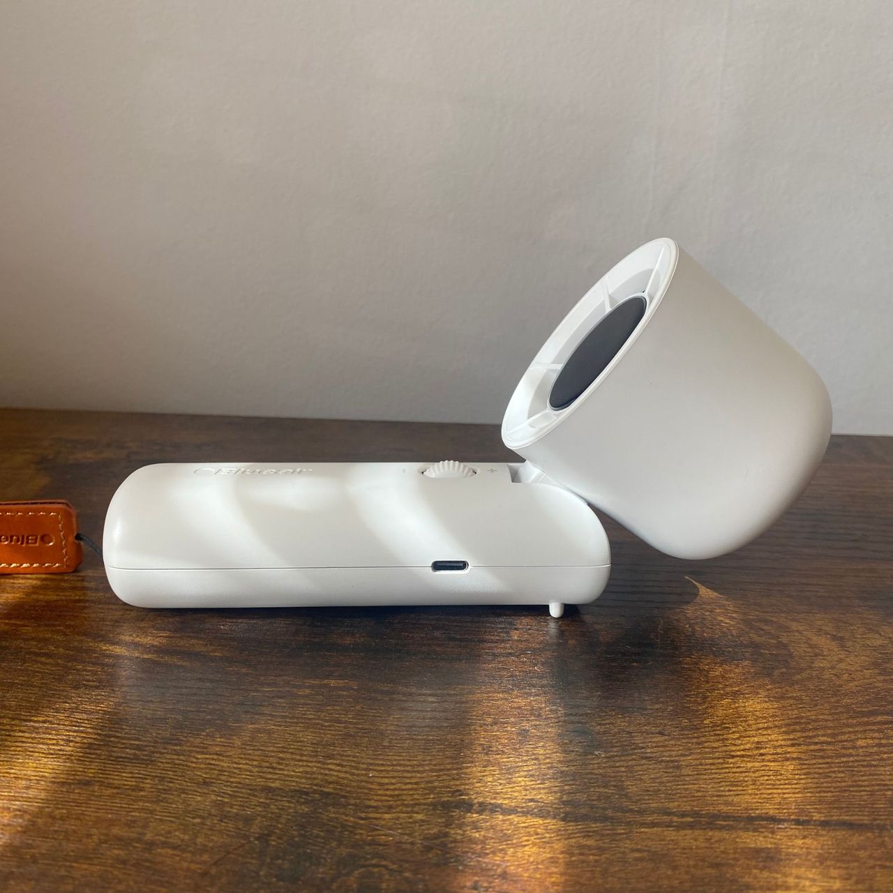 Side view of the Blueair AlwaysCool Portable Handheld Fan laid horizontally with the head tilted forwards on a wood-look surface