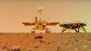 a four-wheeled robot on orange soil next to a hexagonal lander with four triangular legs