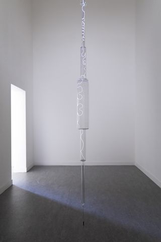 Glass lamp showing electricity running through it placed in the center of a room featuring white walls and grey floors