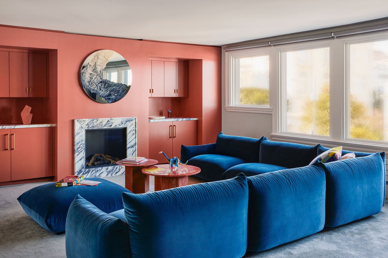 A large light filled family room with an accent pink wall and blue sofa