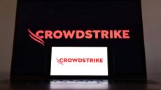 CrowdStrike logo and branding pictured on a tablet screen in red lettering on a black background, with logo on smartphone screen in foreground in red lettering with white background.
