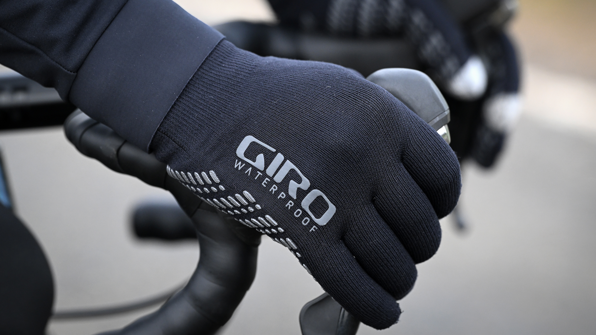 Closeup of hands wearing black gloves with the words 'Giro Waterproof' on them, holding some handlebars