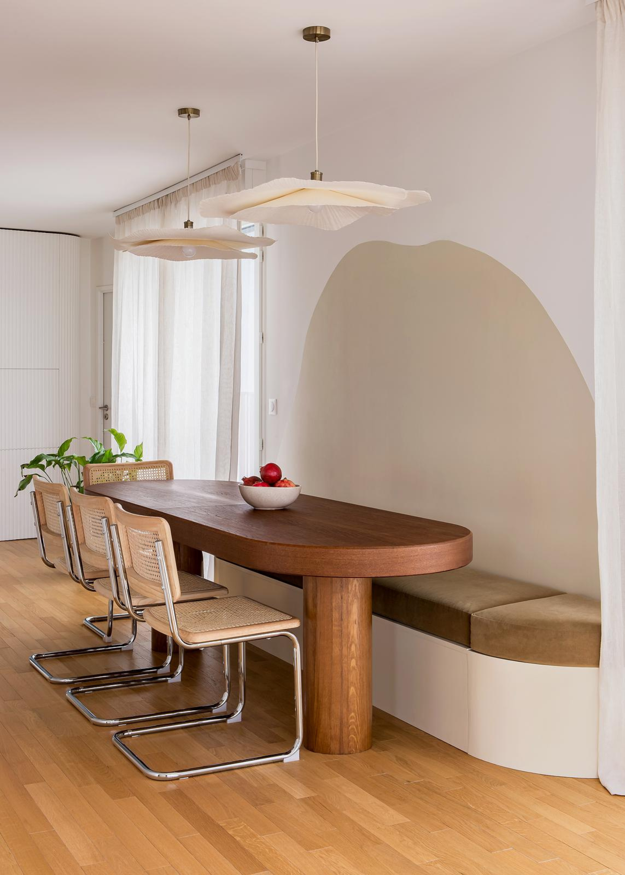 A dining room with an in-built bench, rattan and metal chairs, a wooden dining table and pendant lights