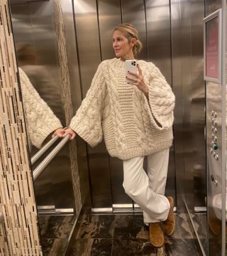 Actress Kelly Rutherford wearing brown Ugg boots, a white cable-knit sweater, and white pants.