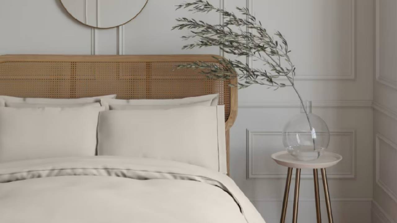 A modern, neutral, panelled bedroom wall with a rattan headboard and luxurious, cream bedding from M&S. 