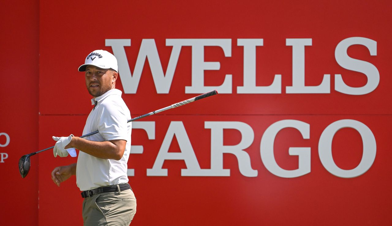 Xander Schauffele takes off his glove in front of a Wells Fargo board