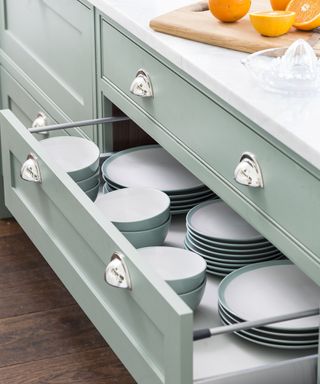 Green kitchen drawers with silver handles storing crockery
