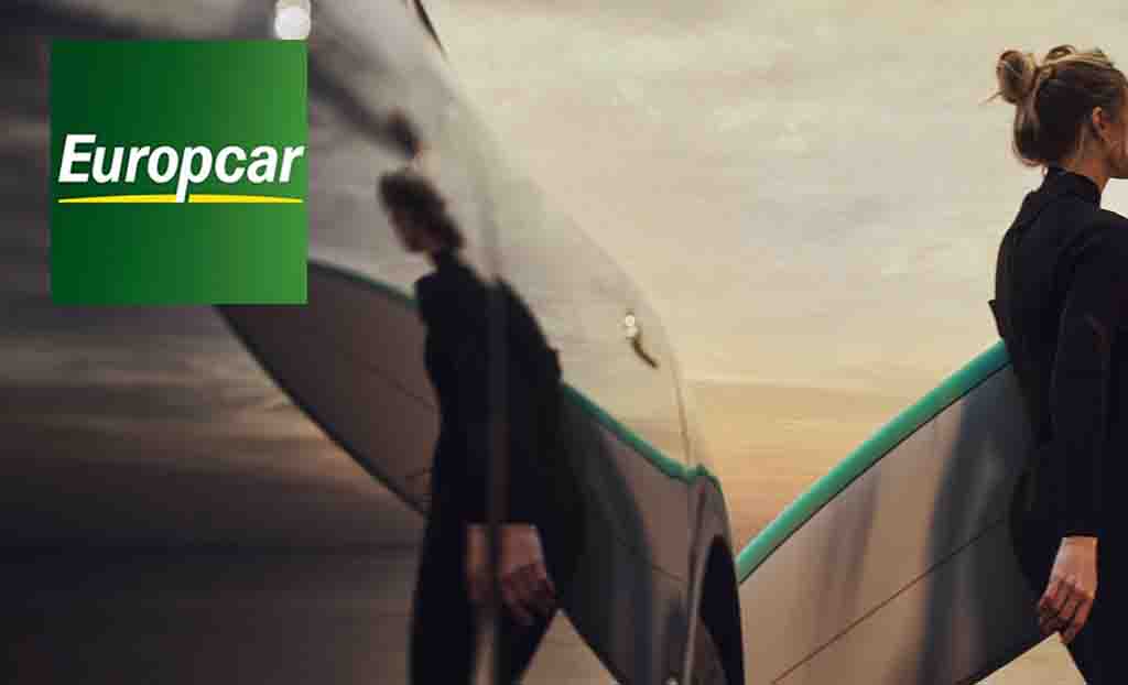 Europcar logo placed over a low angle shot of a woman carrying a surfboard with her reflection in the car 