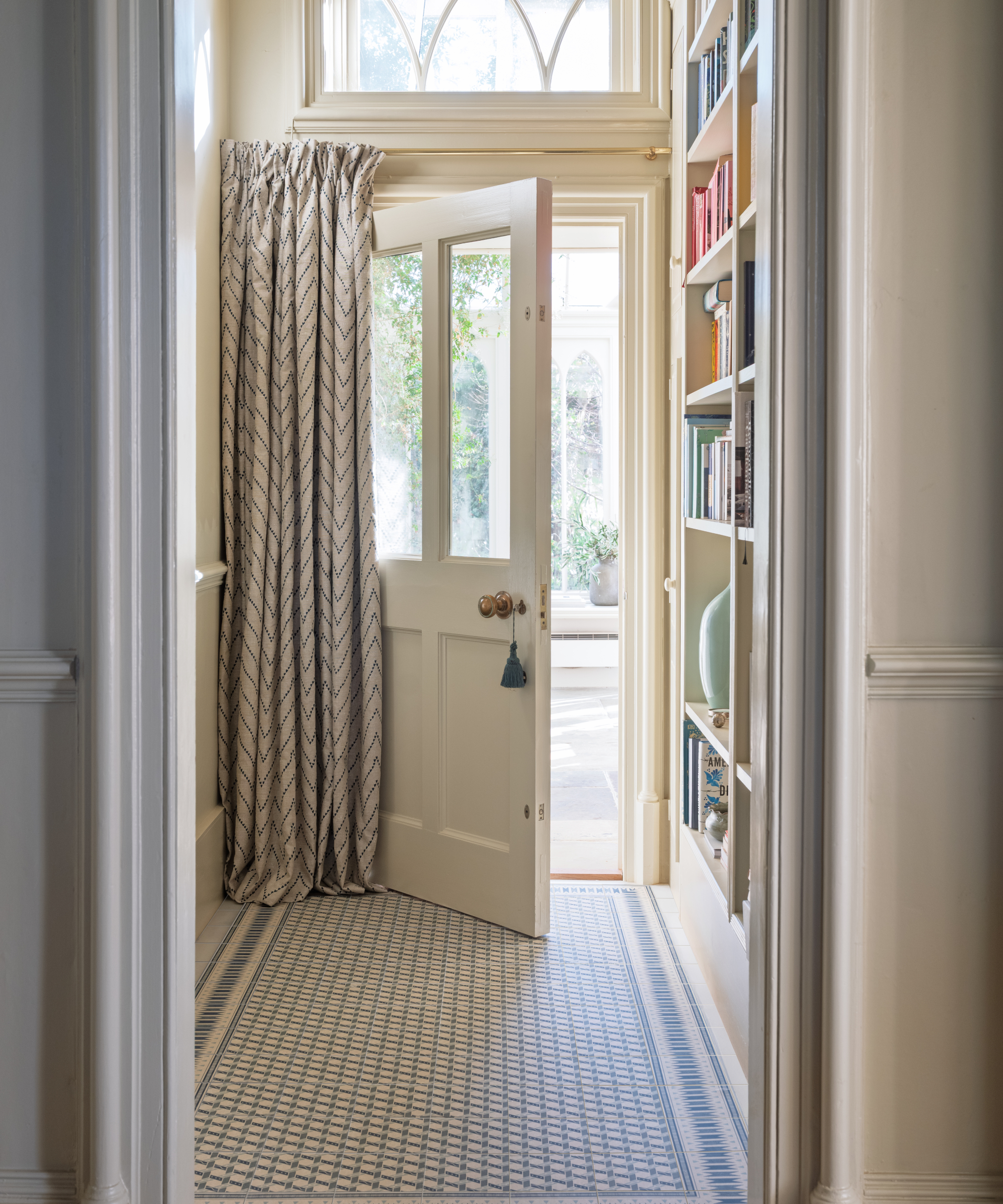 narrow hallway with blue and white tiled floor, curtain in front of door and shallow floor to ceiling storage