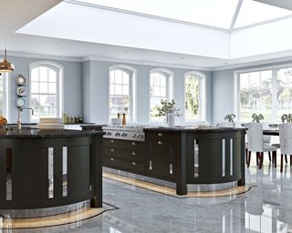 A large kitchen extension with two dark green islands on a high gloss gray floor below a large glass ceiling