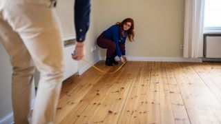 two people measuring a floor in a room