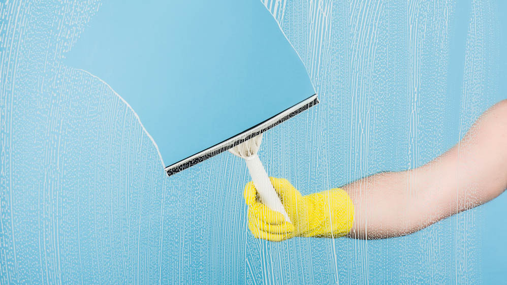 Someone cleans the glass with a squeegee while wearing rubber gloves