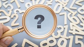 Closeup hand holding a magnifying glass over the wooden numbers