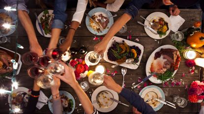 Millennial&#039;s bringing glasses in to cheers over food at a dinner party