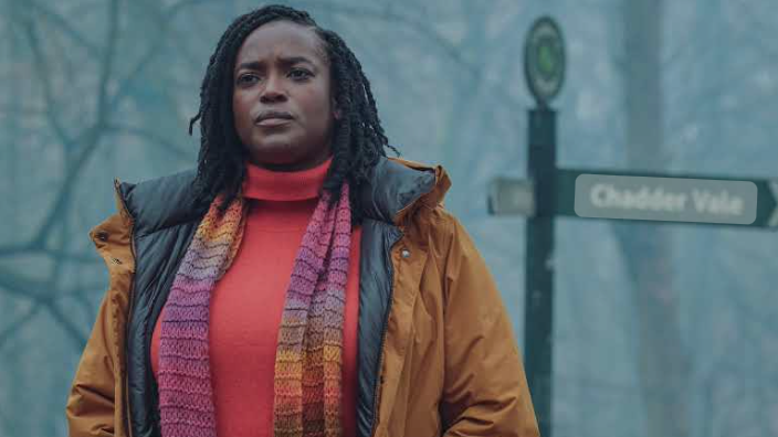 D.I. Riya Ajunwa (played by Wunmi Mosaku) standing in a frosty wooded area by a road sign pointing to Chaddar Vale 