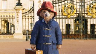 Paddington bear standing in front of the gates of Buckingham Palace.