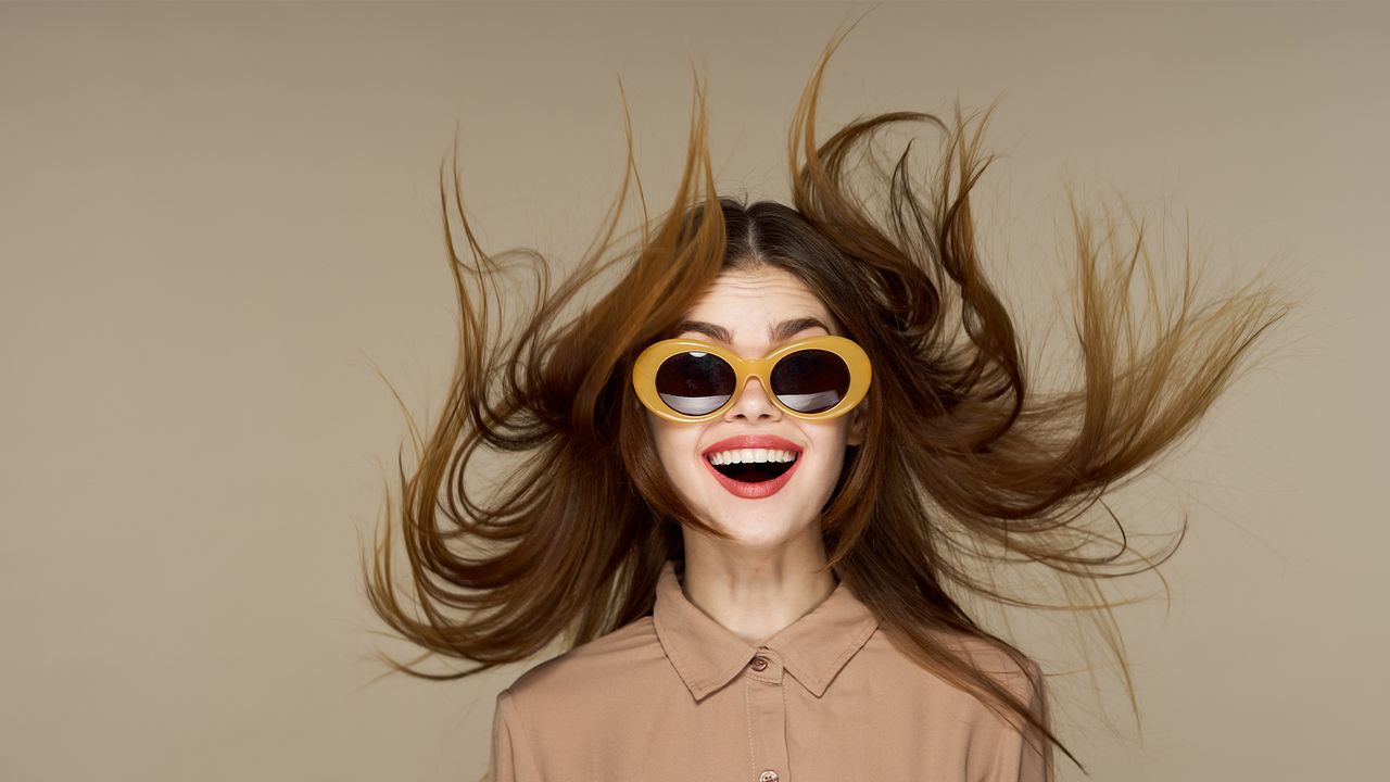 Beautiful fashion woman in round glasses with a surprised expression, flying hair