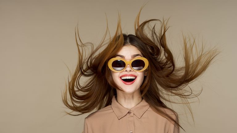 Beautiful fashion woman in round glasses with a surprised expression, flying hair