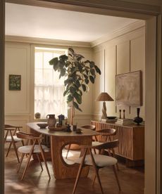 Panelled dining room with wood scandi dining table and chairs, wood side board with lamp and large plant