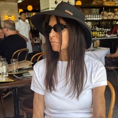 nikki's mom wears a white tank and a black hat.