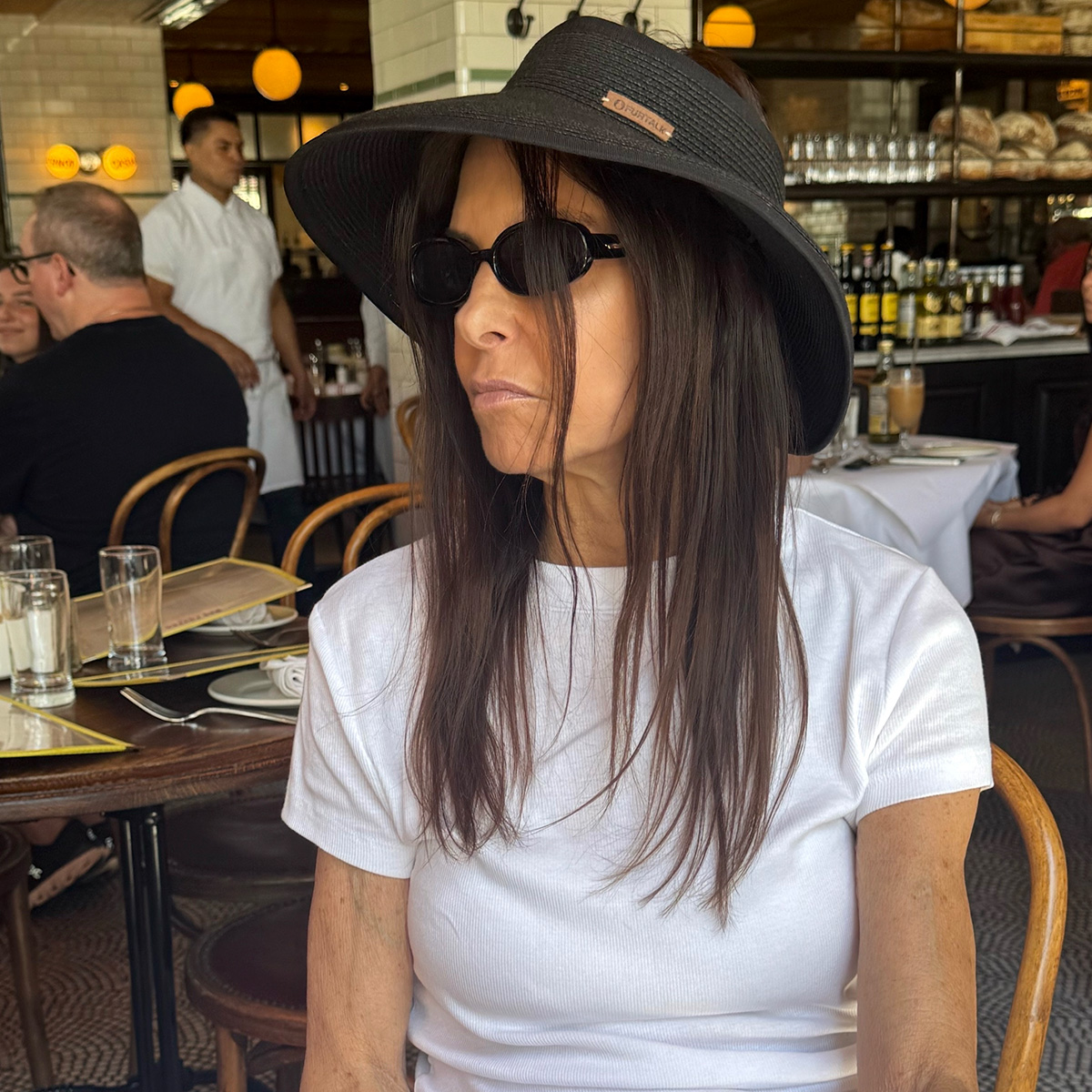 nikki's mom wears a white tank and a black hat.