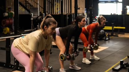 Three women in a gym exercising with dumbbells