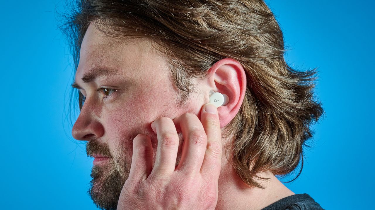 The Soundcore Sleep A30 earbuds in a man's ear. He is reaching a finger up to touch the controls.