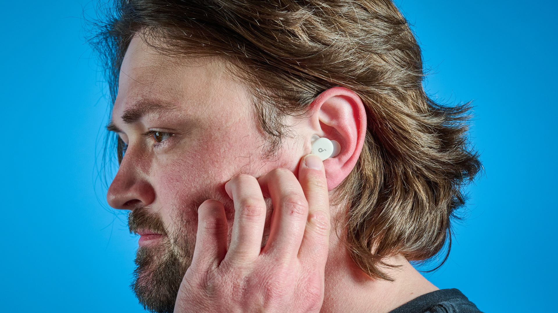 The Soundcore Sleep A30 earbuds in a man&#039;s ear. He is reaching a finger up to touch the controls.