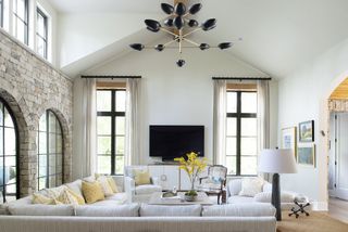 large white living room with black retro pendant, sectionals, yellow accents of seat pillows, exposed brick wall, light and airy, tv