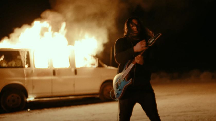 Misha Mansoor plays his signature Jackson Juggernaut in front of a flaming van in a still from the promo video for his signature Neural DSP plugin.