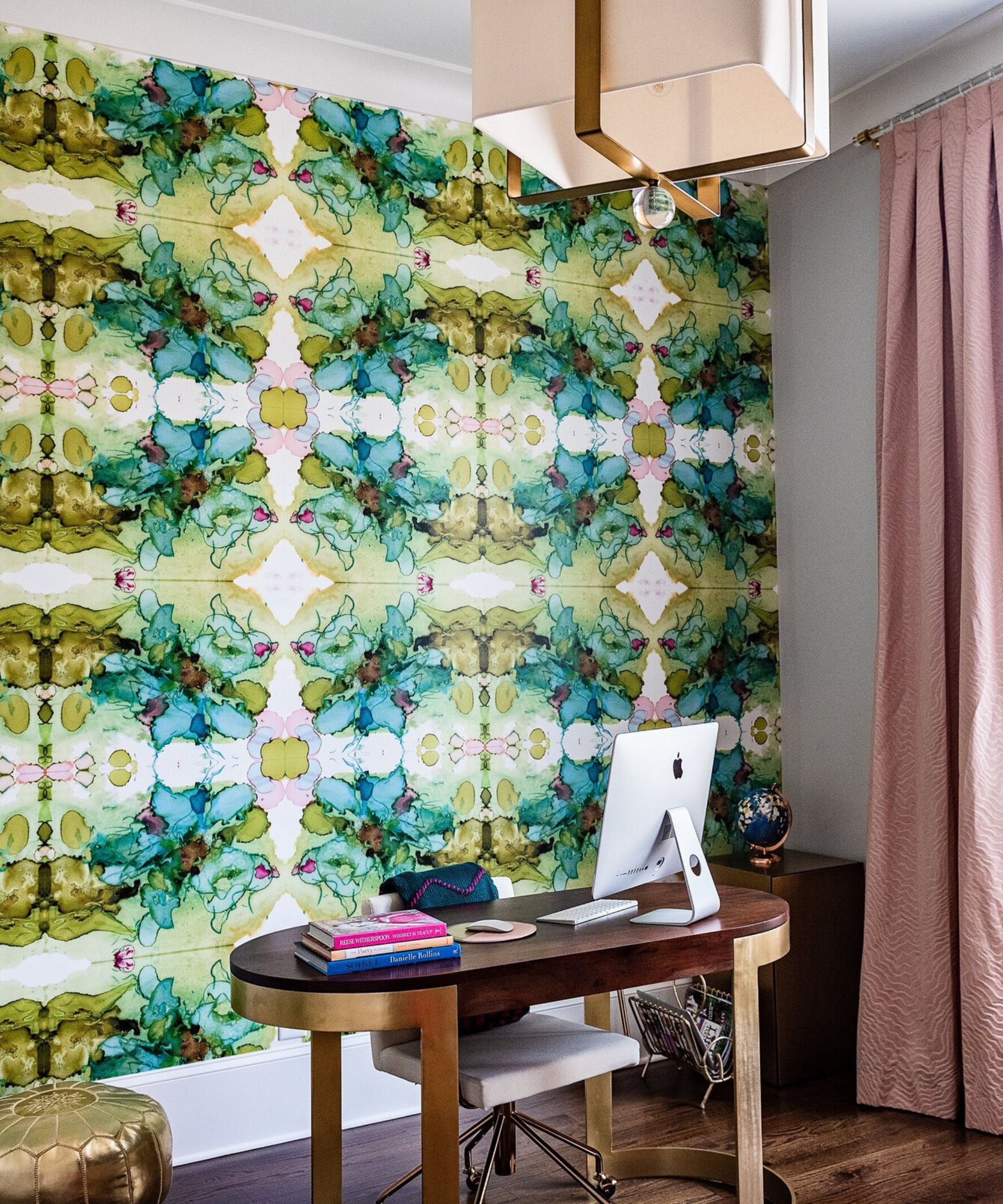a maximalist home office with a bold wallpaper, a wood desk, a macbook, and some books on the desk
