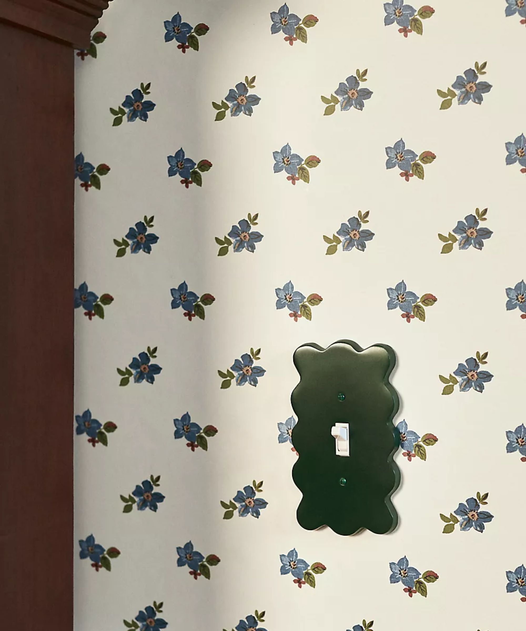 bedroom with blue floral ditsy wallpaper with a dark wooden wardrobe and a dark green wiggle scalloped shaped light switch plate
