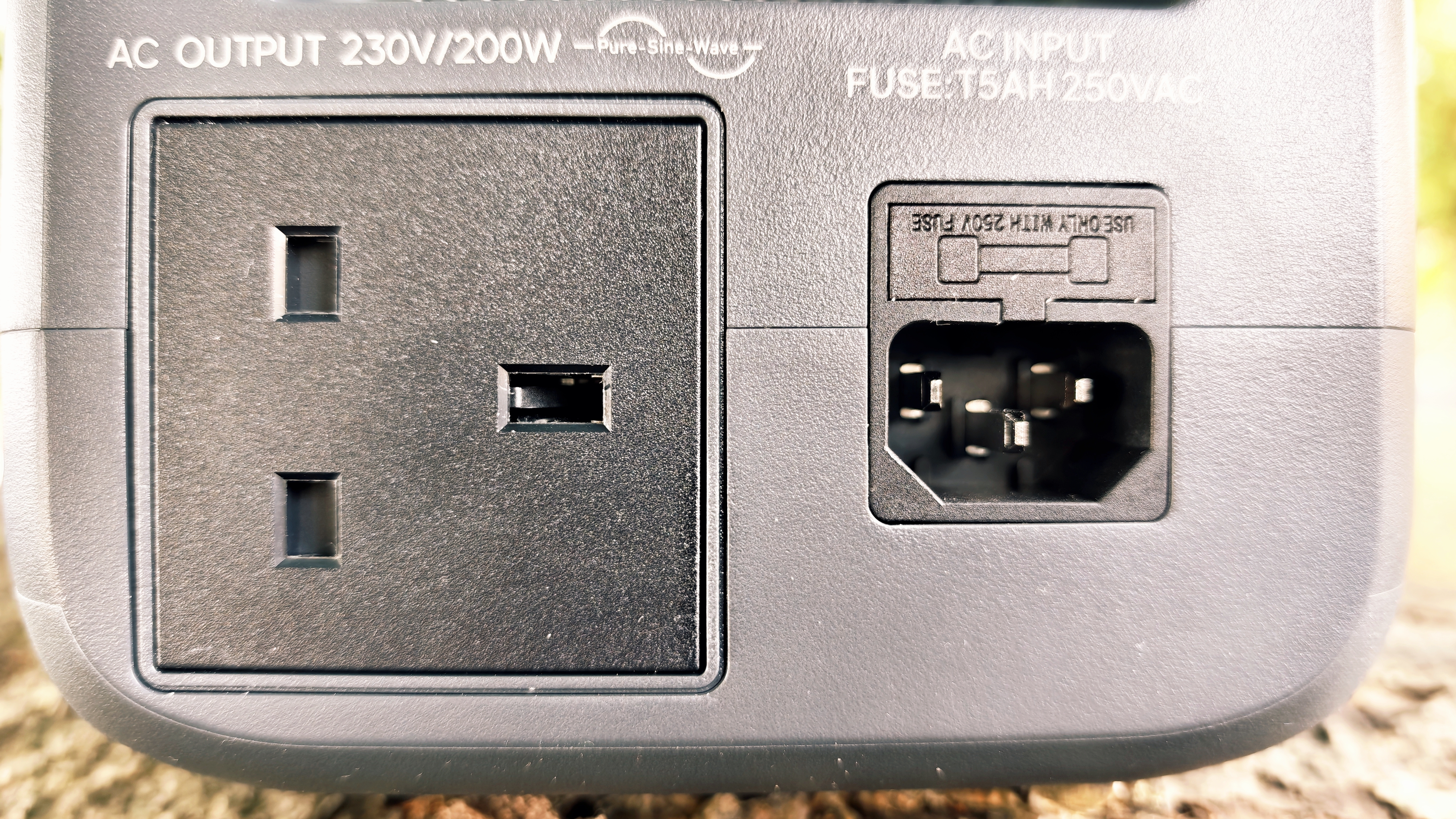 A grey Bluetti Elite 10 power station sitting on a log in a forest grove