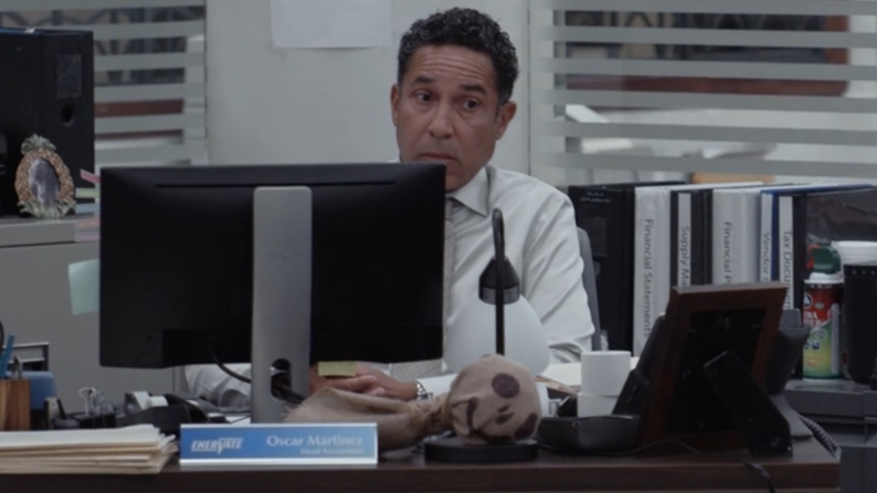 Oscar seated at his desk looking wary in The Paper
