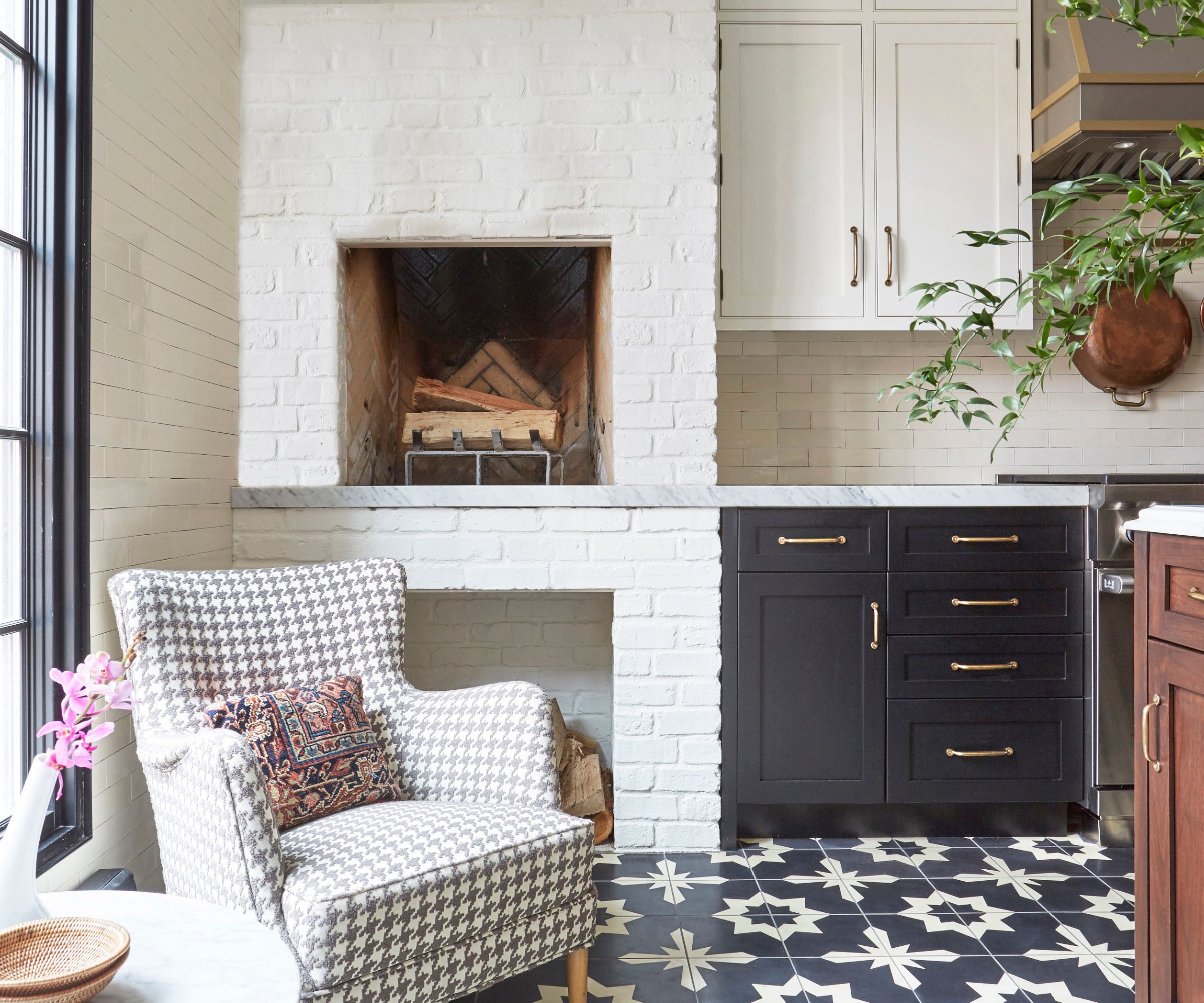 A cozy kitchen corner with a brick fireplace and a reupholstered antique armchair in a dogtooth print