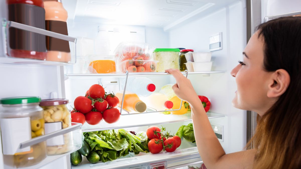 A woman looking in a fridge stacked full of food