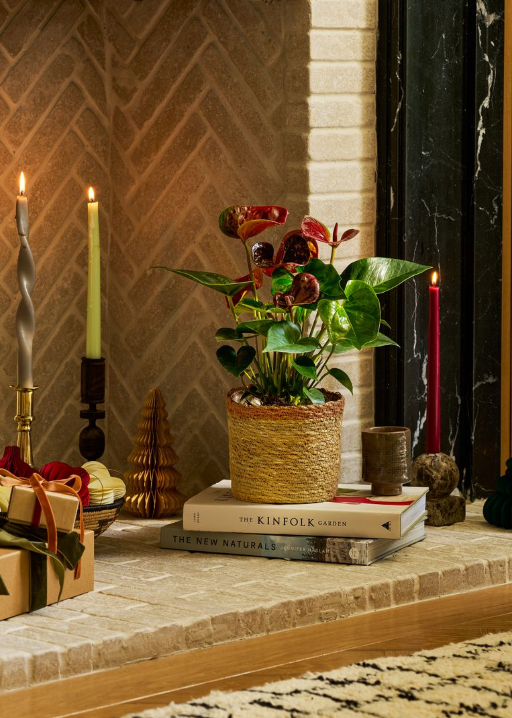 A red anthurium in a woven planter on a stack of books in a fireplace by candles