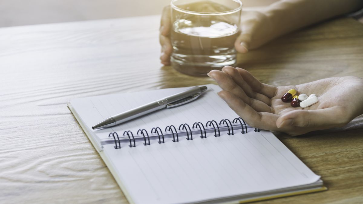 Nootropics: Close up image of a hand holding pills above a notepad and pen on a desk.