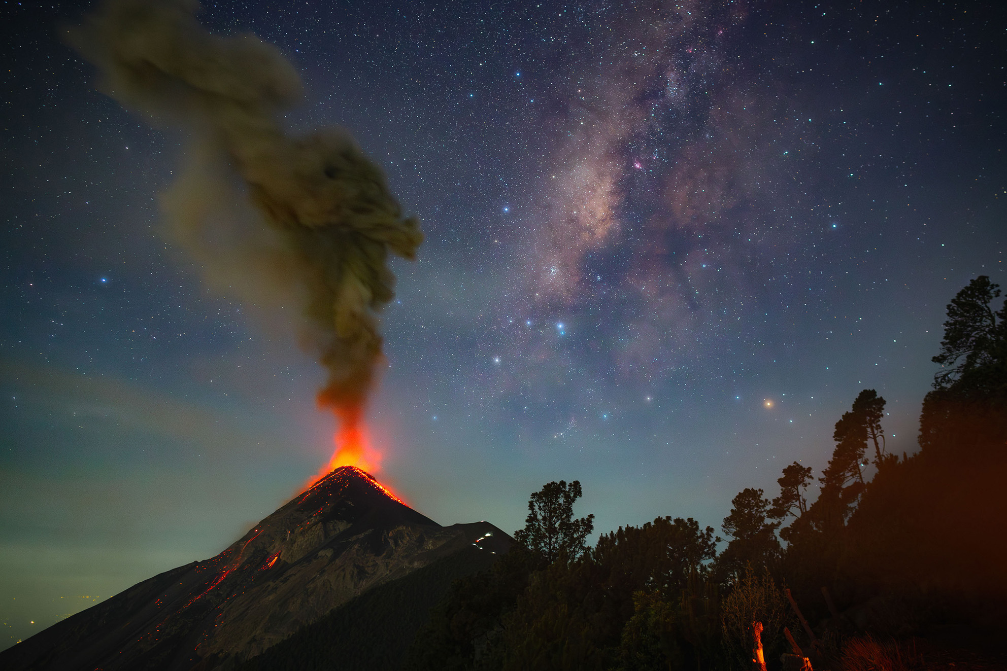 A vibrant volcano erupts under a starry night sky, with glowing lava and smoke billowing upwards, creating a stunning natural spectacle