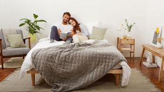 Mela Original Weighted Blanket review: a couple relax in bed with the Mela Original Weighted Blanket in grey draped over the bottom